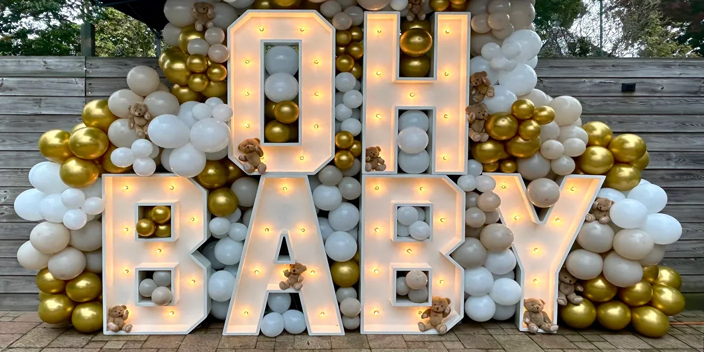 Lichtletters met de tekst “OH BABY” voor een backdrop van witte en gouden ballonnen met teddyberen, gebruikt als styling voor een babyshower.